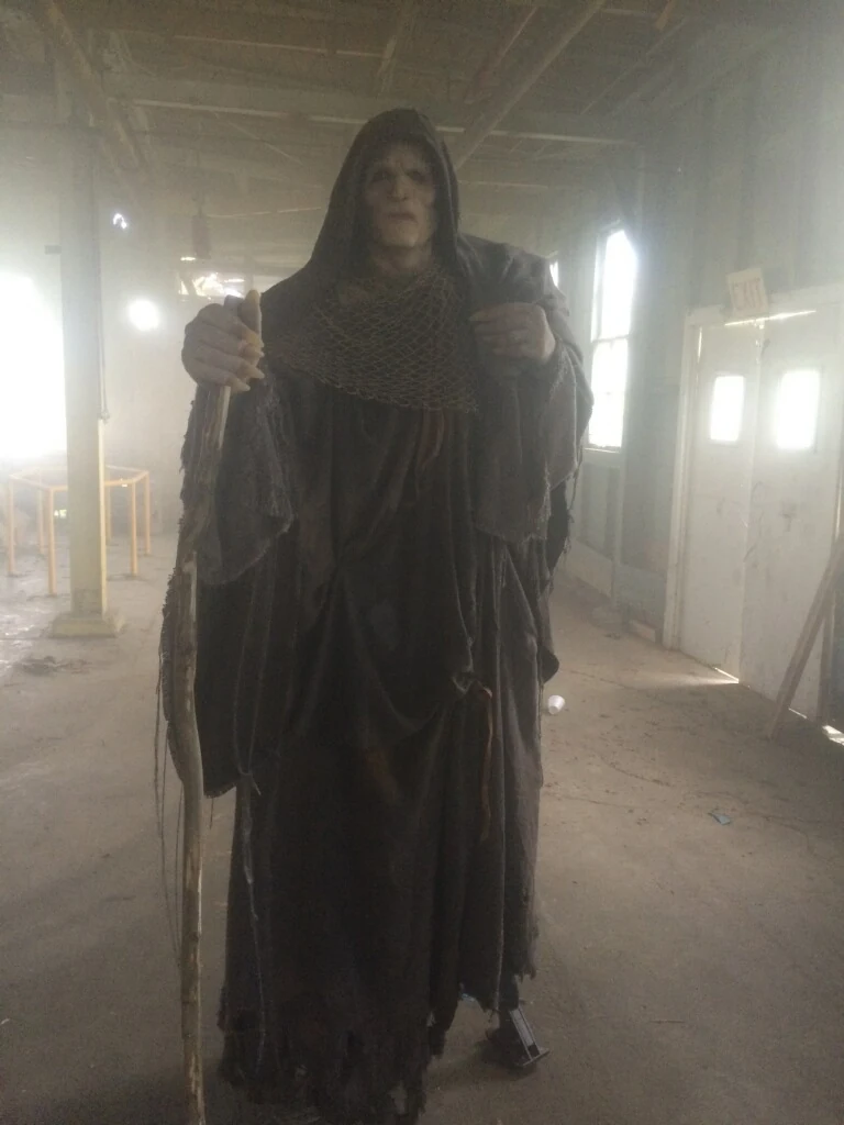 Performer in a dark hooded creature costume on set